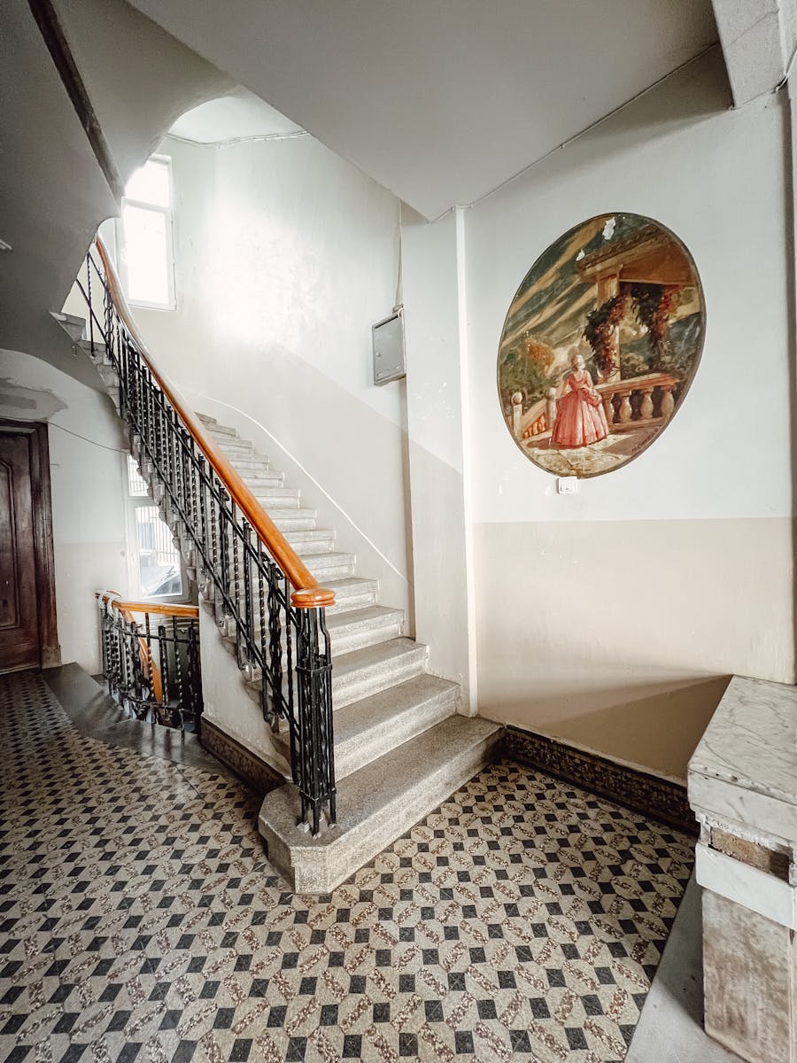 A classic indoor setting featuring a decorative staircase and a mural painting on the wall.