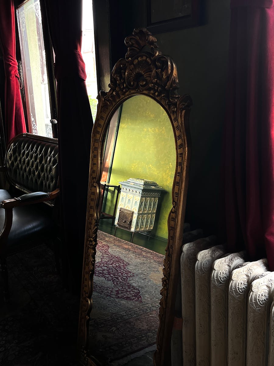 A vintage ornate mirror reflecting a dollhouse in a dimly lit room with classic decor.